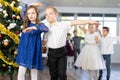 Little children practicing waltz dance in school-hall decorated with Christmas-tree