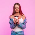 Joyful modern beautiful young woman in youth stylish jeans clothes holds cup of coffee in hands and looks down indoors. Happy