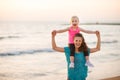 Joyful mother holding daughter on shoulders on beach at sunset Royalty Free Stock Photo