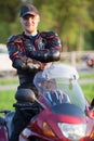 Joyful motorcyclist standing on his bike. Safety equipment as protector jacket