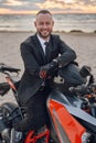 Joyful motorcyclist in suit riding sports bike on beach