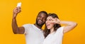 Joyful multiracial couple capturing selfie on smartphone, having fun together