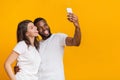Joyful multiracial couple taking selfie on smartphone, grimacing and showing tongues