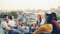Joyful musician is playing the guitar with his friends singing and laughing sitting on rooftop at table. Entertainment Royalty Free Stock Photo