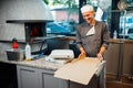 Joyful pizzeria worker makes a pizza box. Catering kitchen work.