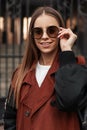 Joyful portrait urban girl with positive smile in trendy clothes outdoors. Happy young hipster woman in stylish trench coat puts Royalty Free Stock Photo