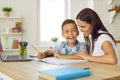 Joyful preschooler boy is studying and writing in notebook at home with help of his mother.