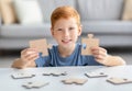 Joyful preteen boy holding two pieces of wooden puzzles