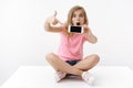 Joyful pretty amused teenage blond girl with cute surprised expression sit on floor, show blank smartphone screen Royalty Free Stock Photo