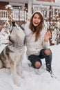 Joyful pretty girl in winter clothes playing with husky dog in snow. Fashionable young woman enjoying cold winter Royalty Free Stock Photo