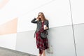 Joyful pretty stylish woman in trendy red-black youth clothes from new summer collection with cup of tea poses near modern wall on Royalty Free Stock Photo