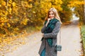 Joyful pretty young happy woman in stylish warm seasonal clothes with a leather handbag is standing and smiling on the road