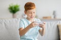 Joyful redhead boy playing video games, using cellphone