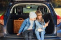 Joyful 12-s brother and sister taking selfie photos on smart phone sitting in the opened car`s trunk. Royalty Free Stock Photo