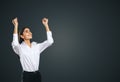 Joyful and satisfied woman in white shirt with raised hands showing her power, winner and achievement concept, isolated on dark Royalty Free Stock Photo