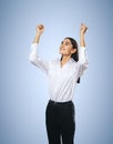 Joyful and satisfied woman in white shirt with raised hands showing her power, winner and achievement concept, isolated on light Royalty Free Stock Photo