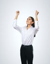 Joyful and satisfied woman in white shirt with raised hands showing her power, winner and achievement concept, isolated on light Royalty Free Stock Photo