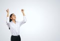 Joyful and satisfied woman in white shirt with raised hands showing her power, winner and achievement concept, isolated on light Royalty Free Stock Photo