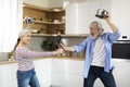 Joyful senior spouses having fun together in kitchen, playfully fighting with kitchenware Royalty Free Stock Photo
