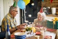 Joyful senior woman blowing candles on birthday cake, sitting at the kitchen table with her husband, celebrating her birthday Royalty Free Stock Photo