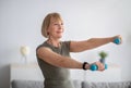 Joyful senior woman doing domestic training, working out with dumbbells, exercising her biceps at home Royalty Free Stock Photo