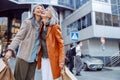Joyful senior woman with shopping bags hug Asian lady on modern city street Royalty Free Stock Photo