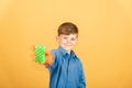 A joyful and smiling boy in a blue shirt and orange gloves shows a washing sponge in green on a yellow background Royalty Free Stock Photo