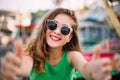 Joyful smiling girl in pink sunglasses making selfie in front of carousel. Outdoor portrait of cute stylish woman having fun in am Royalty Free Stock Photo
