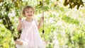 Joyful smiling little girl swinging on the swing, child with blue eyes and curly blond hair plays in the green garden at home, Royalty Free Stock Photo