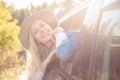 Joyful smiling thoughtful blond woman in hat and jeans suit leaning out of car window joy summer trip nature in sunlight Royalty Free Stock Photo