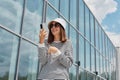 Joyful smiling woman wearing striped shirt using phone posing near building with big windows making selfie on her cell phone Royalty Free Stock Photo