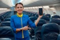 Joyful stewardess with smartphone standing in airplane cabin Royalty Free Stock Photo