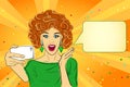 Joyful surprised woman with red hair, open mouth, with mobile phone in her hand, green shirt, orange background Royalty Free Stock Photo