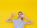 Joyful teen girl with headphones smiling showing peace gesture over yellow background, copy space Royalty Free Stock Photo