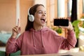 Joyful teen girl singing song and using smartphone as microphone, wearing wireless headset, having fun at home Royalty Free Stock Photo