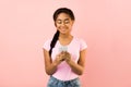 Joyful teen girl texting on smartphone on pink background