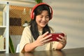 Joyful teenage asian girl playing video game on a portable game console at home. Leisure, entertainment and technology Royalty Free Stock Photo