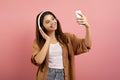Joyful teenage girl wearing wireless headphones taking selfie on smartphone Royalty Free Stock Photo