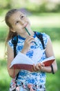 Joyful thoughtful girl stands in summer park with sketchpad and color pencil in hands, portrait