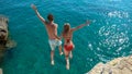Joyful tourist couple decides to jump off a rocky cliff and dive into sea.