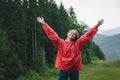 Joyful tourist girl standing in mountains in rainy weather against beautiful landscape background, looking into camera and smiling Royalty Free Stock Photo