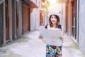 Joyful tourist young woman holding paper map direction while walking in city street. Traveler girl finding some way reading map in