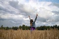 Joyful victorious young woman celebrating life as she stands with her arms raised high towards a dramatic cloudy sky