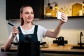 Joyful woman in an apron cooks at home and tastes a dish, shooting a video tutorial on the phone in the kitchen interior Royalty Free Stock Photo