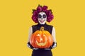 Joyful woman with creative traditional Mexican make-up holding glowing Halloween pumpkin.