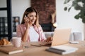 Joyful woman having a phonecall and checking updates on laptop