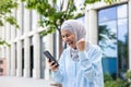 Joyful woman in hijab walking in the city, received notification of online win and good news on phone, business woman Royalty Free Stock Photo