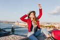 Joyful woman with light-brown hair happy waving hands while posing on city background. Dreamy female tourist with red