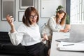 Joyful woman office worker in headphones listening music and pretend playing guitar, colleague sitting at desk Royalty Free Stock Photo