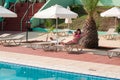 Joyful woman resting under sunshade in shadow close to swimming pool in a hotel area